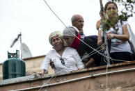 A woman cries as she stands with others on the roof of an abandoned school before being evicted, on the outskirts of Rome, Monday, July 15, 2019. Residents set fire early Monday to mattresses and other garbage to form a barrier and prevent riot police from entering the building but authorities doused the blaze and proceeded with the eviction. (Massimo Percossi/ANSA via AP)