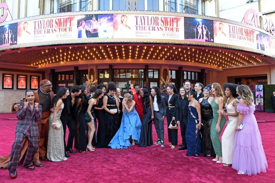 Taylor Swift in a blue dress on a red carpet among several people outside a movie theater