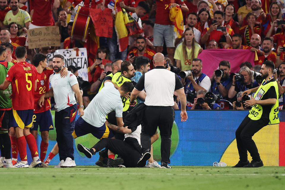 A security member slides into Spain player Alvaro Morata as he attempts to remove a pitch invader.