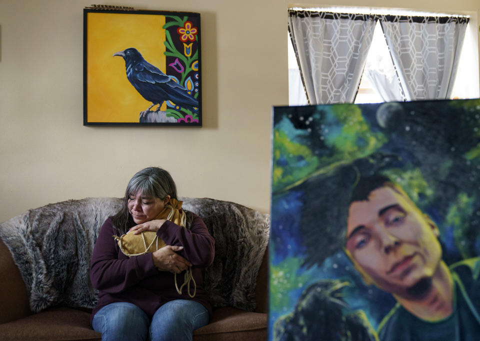 Rachel Taylor clutches a buckskin satchel filled with the ashes of her son, Kyle "Little Crow" Domrese, pictured at right, who died of an overdose, as she sits in the home they shared in Bemidji, Minn., Wednesday, Nov. 17, 2021. Just weeks remained until the anniversary of the day she opened his bedroom door and found her son face-down on his bed, one of more than 100,000 Americans lost in a year to overdoses as the COVID-19 pandemic aggravated America's addiction disaster. The death rate from drug overdoses for Native Americans has surpassed white people and is now the highest in the nation. (AP Photo/David Goldman)