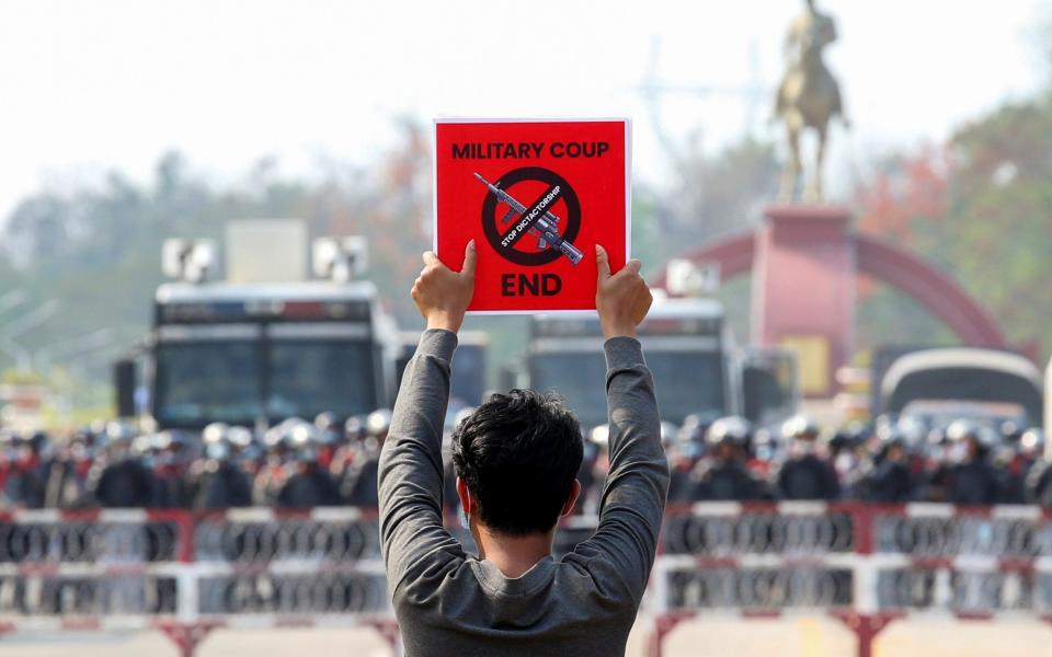 A demonstrator holds a placard in front of a police line, Feb 18, 2021 - Reuters