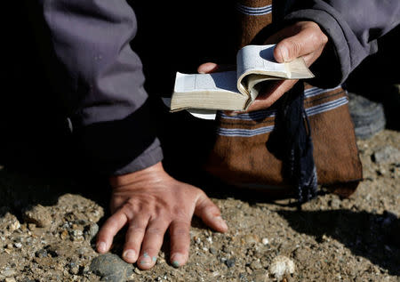 A relative reads the holy book Quran on the grave of one of the victims, who was killed during yesterday's suicide attack at Shi'ite cultural centre in Kabul, Afghanistan December 29, 2017. REUTERS/Omar Sobhani