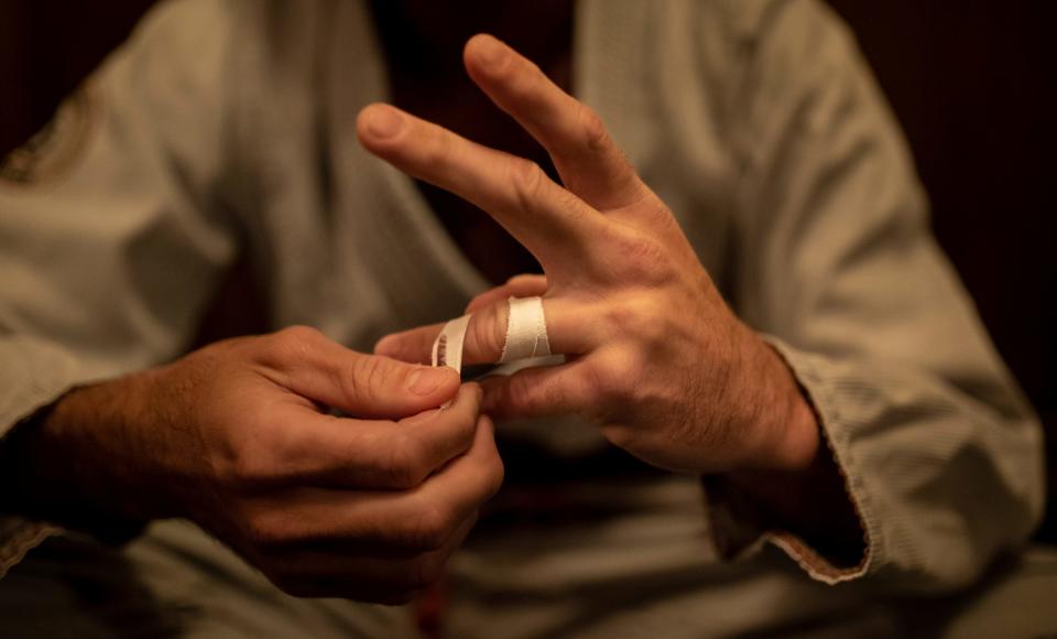 Zach Mabey, 31, a brown belt in Brazilian jujitsu, adds strips of tape around his fingers as he prepares for his match during the Grapple in the Temple jujitsu tournament at the Masonic Temple in Detroit on Friday, Aug. 11, 2023.