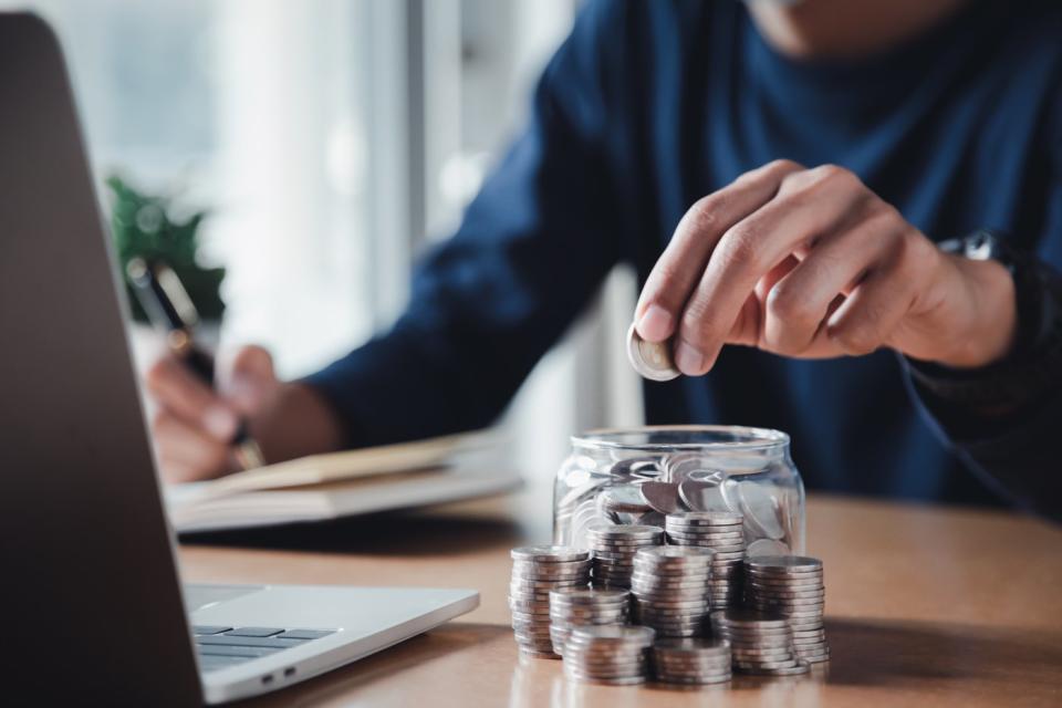 Someone writing on a notepad while putting a coin in a jar.