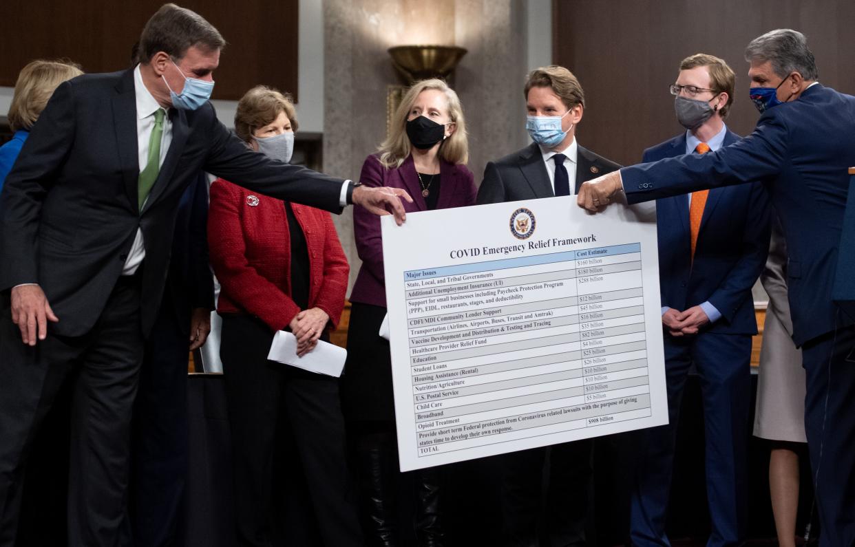 Senator Joe Manchin (R) hands a poster describing a proposal for a Covid relief bill to Senator Mark Warner (L), alongside a bipartisan group of members of Congress (AFP via Getty Images)