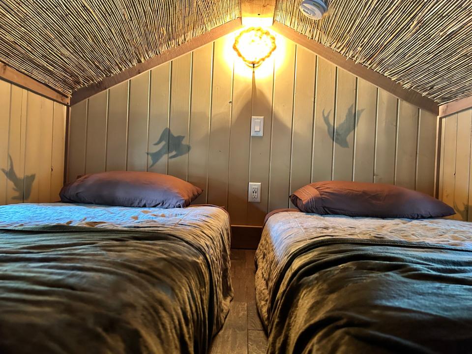 top floor bed with birds on wall, thatched ceiling, two beds