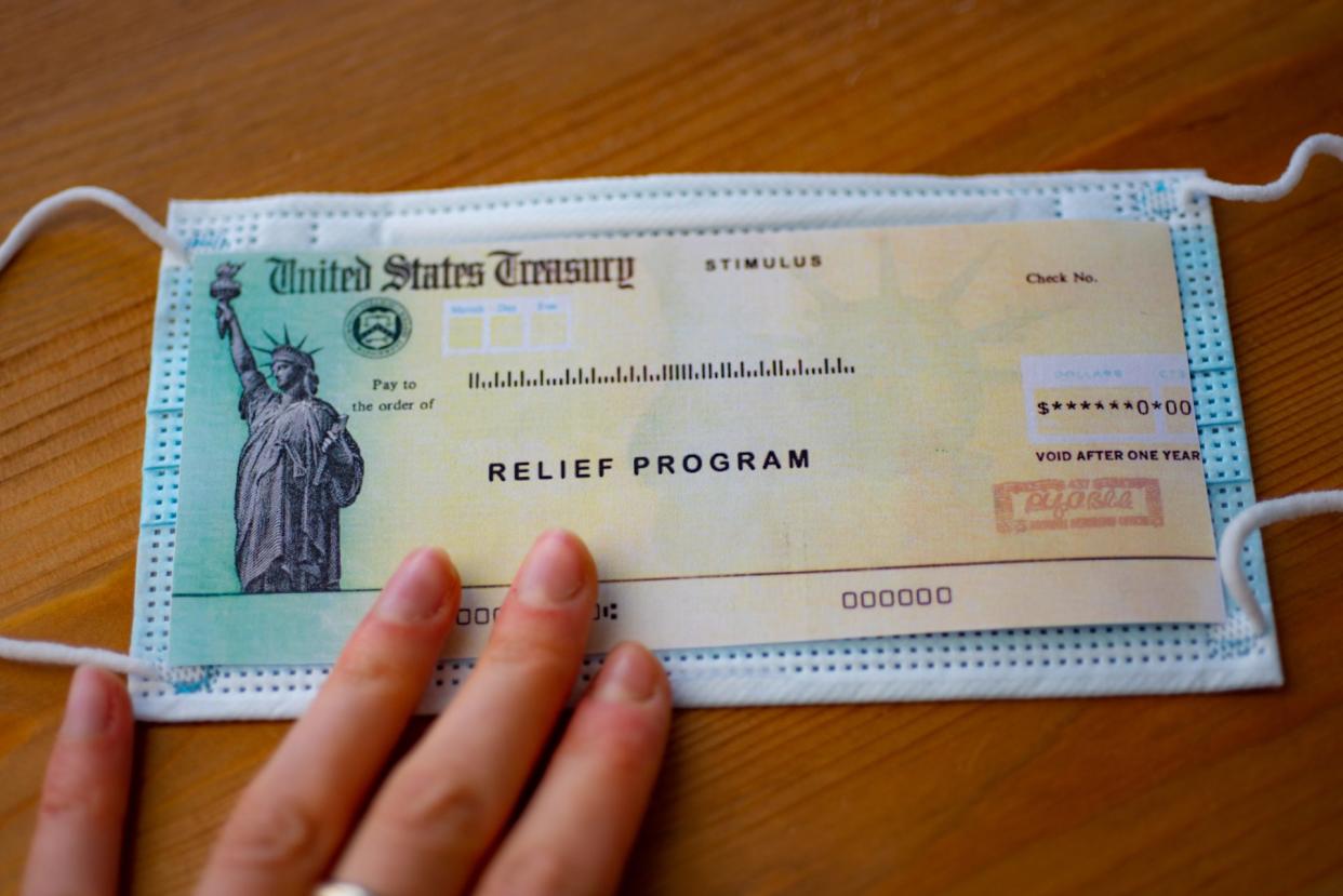 Stimulus relief program check over medical mask on wooden surface.