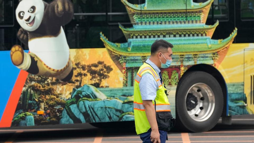 Ein Verkehrspolizist steht bei Probefahrten neben einem Bus, auf dem für den Vergnügungspark von Universal Studios geworben wird.