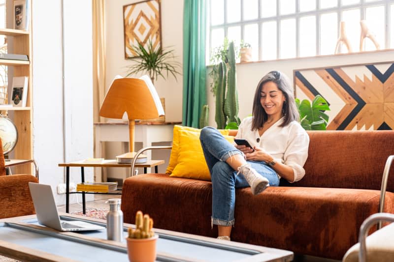 Woman at home sitting on her sofa looking at her cell phone