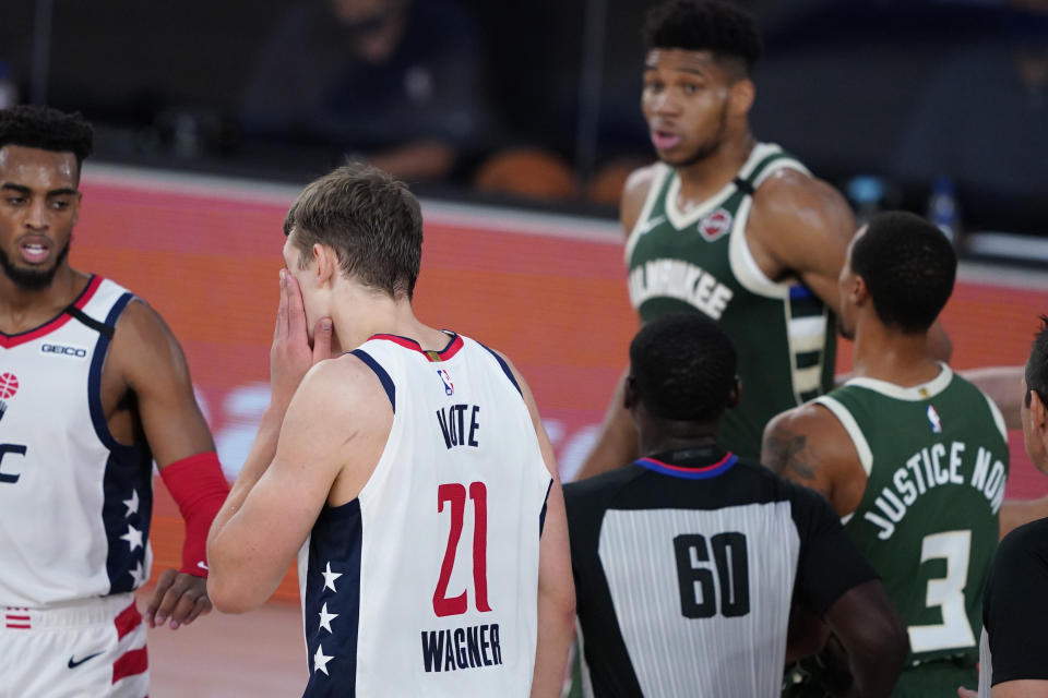 Washington Wizards' Moritz Wagner (21) grabs his face after getting head butted by Milwaukee Bucks' Giannis Antetokounmpo, rear, during the first half of an NBA basketball game, Tuesday, Aug. 11, 2020, in Lake Buena Vista, Fla. Antetokounmpo was ejected from the game. (AP Photo/Ashley Landis, Pool)