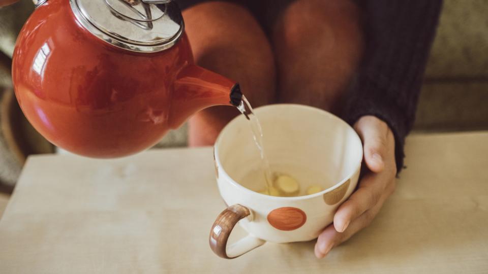 woman pouring water into tea cup with chopped fresh ginger, close up