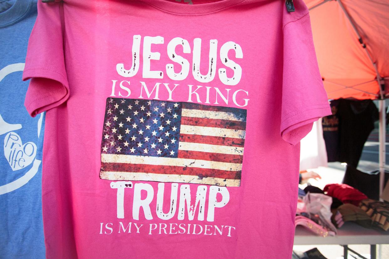 A shirt that reads "Jesus is my king, Trump is my president" hangs at an American Great Store merchandise booth outside the Phoenix Convention Center on day 2 of Turning Point USA's AmericaFest on Dec. 19, 2021.