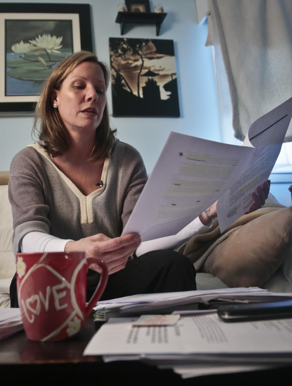 In this March 11, 2014 photo, Nora Milligan looks through a pile of legal healthcare documents at her home in Patchogue, NY. . Milligan, a single mom, is fighting healthcare providers in court for denial of care to her heroin-addicted son. Having exhausted her finances for his care, she continues to live in the home she raised him even as it is being foreclosed. (AP Photo/Bebeto Matthews)