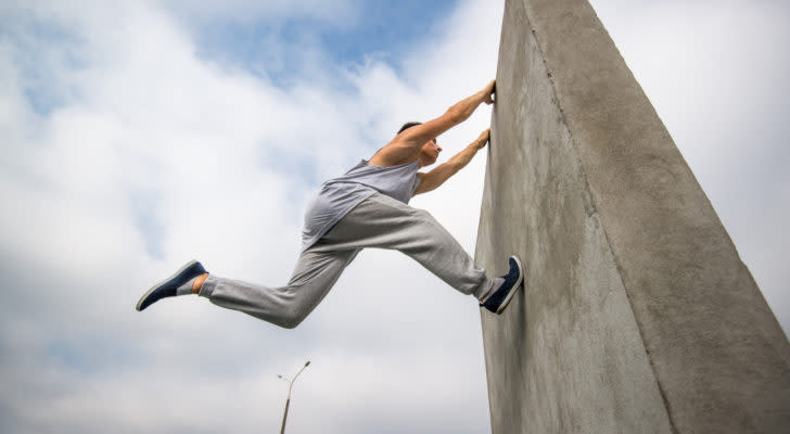 photo of man practicing parkour, jumping on tall cement wall in black sneakers