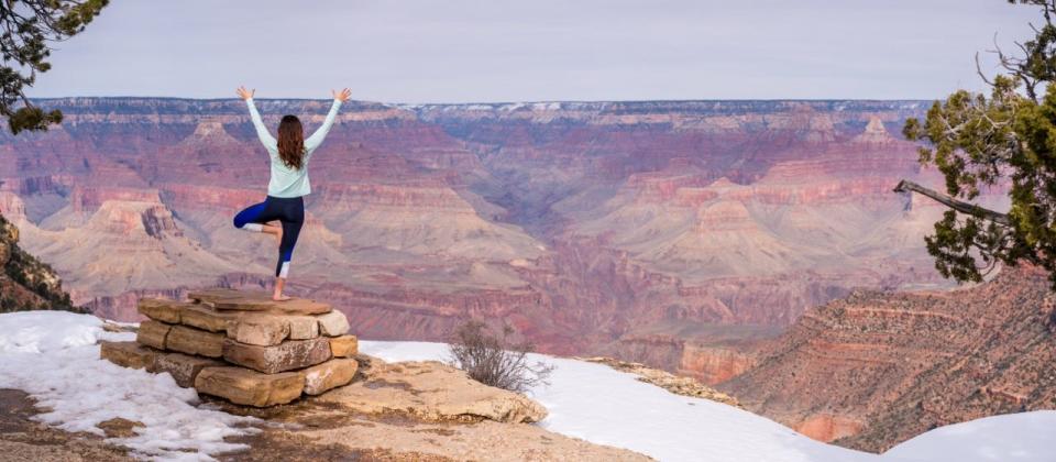 Woman posing in front of the Grand Canyon with her hands in the air on one foot