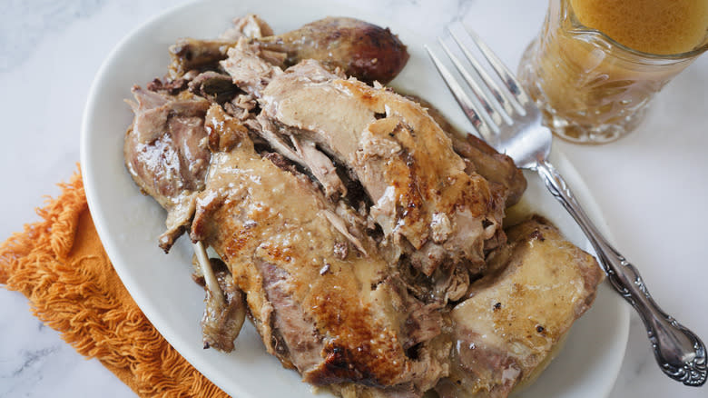 Duck on platter with fork and sauce in background