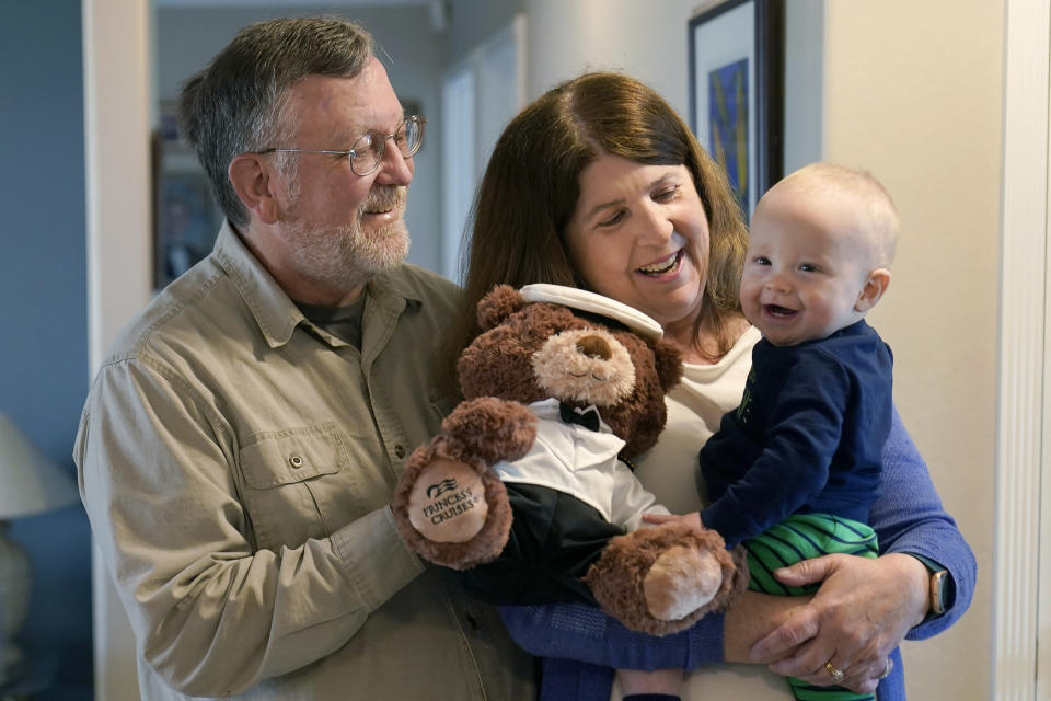 John Miller, left, watches as his wife, Laurie, holds their grandson, Theo Hamilton, while being interviewed in San Jose, Calif., Wednesday, March 10, 2021. The Millers were passengers on the Grand Princess cruise ship, which had captured the world's attention in 2020 when it became clear the coronavirus pandemic had arrived at U.S. shores on board the boat. "There was so much inconsistent information from day-to-day that it felt like we were guinea pigs,” Laurie Miller said. (AP Photo/Jeff Chiu)