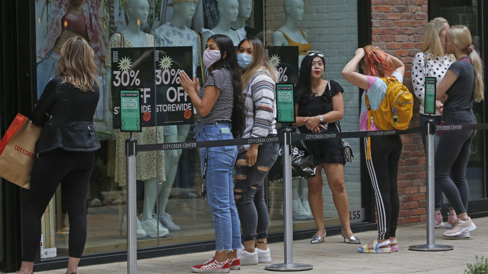 In this May 22, 2020, photo, people wait in line as they stand between social distancing signs in front of Cotton On, at City Creek Center, in Salt Lake City. Utah is seeing a spike in new COVID-19 cases about a month after many businesses were allowed to reopen, leading state health officials to issue renewed pleas for people to maintain social distancing. (AP Photo/Rick Bowmer, File)