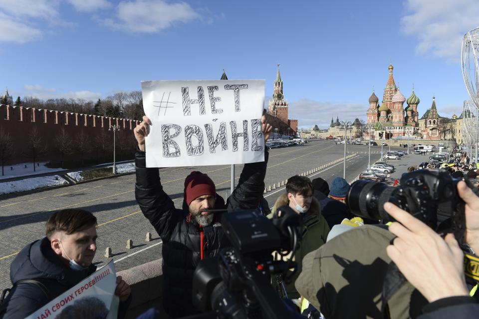 A man holds a poster which reads "No War" as people lay flowers near the place where Russian opposition leader Boris Nemtsov was gunned down, with the Kremlin Wall, left, the Spaskaya Tower, center, and St. Basil's in the background in Moscow, Russia, Sunday, Feb. 27, 2022. (AP Photo/Denis Kaminev)
