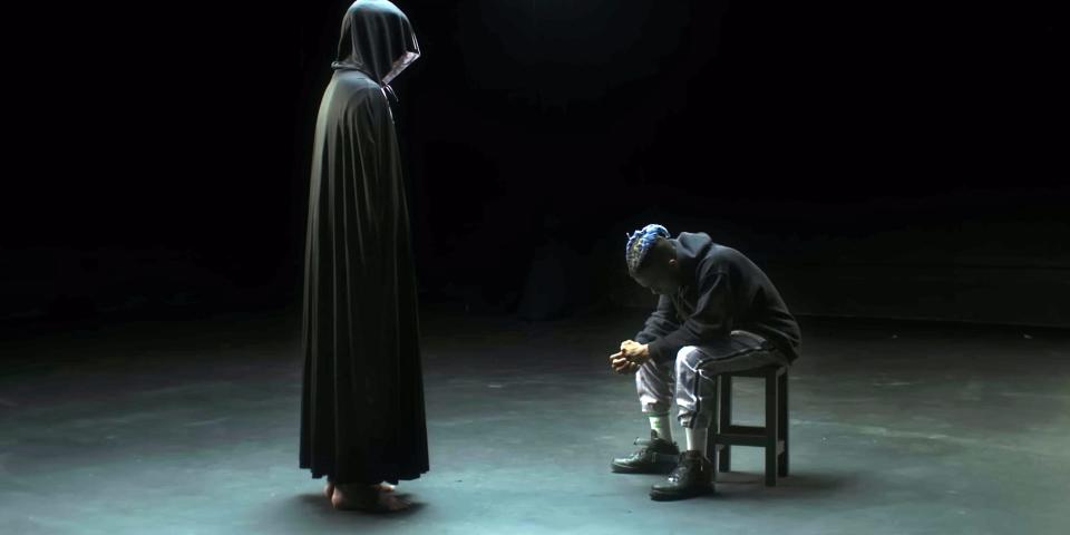 XXXTENTACION sitting down in front of a hooded figure.