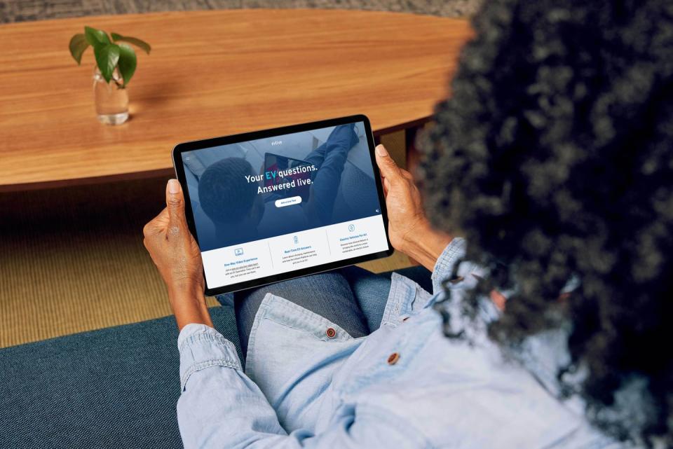 a person sits inside their home, holding a tablet that displays gm’s ev live website