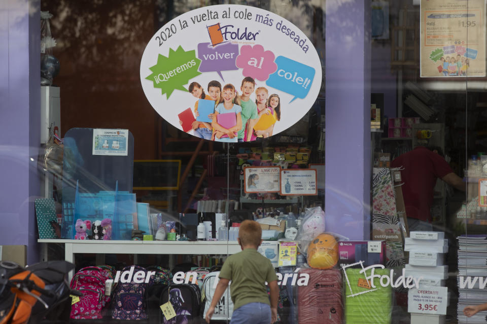 A boy plays in front of a store selling children's school stationery, backpacks, protective masks and hand sanitizers in Madrid, Spain, Monday, Aug. 24, 2020. Poster in Spanish reads '2020, the return to school most wished for. We want to go back to school'. Despite a spike in coronavirus infections, authorities in Europe are determined to send children back to school. Schools in the Spanish capital are scheduled to open on Sept. 4. (AP Photo/Paul White)