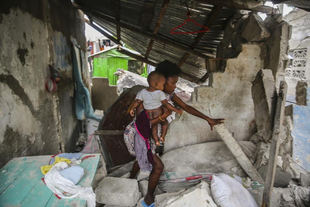 A woman carries her child as she walks in the remains of her home destroyed by Saturday´s 7.2 magnitude earthquake in Les Cayes, Haiti, Sunday, Aug. 15, 2021. (AP Photo/Joseph Odelyn)