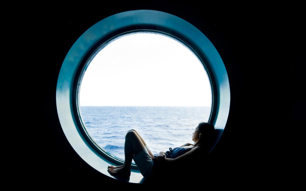 Girl daydreaming at a porthole - Getty