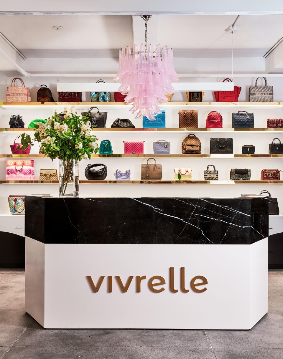 The concierge bar at the Vivrelle showroom has a backdrop of designer bags behind it.