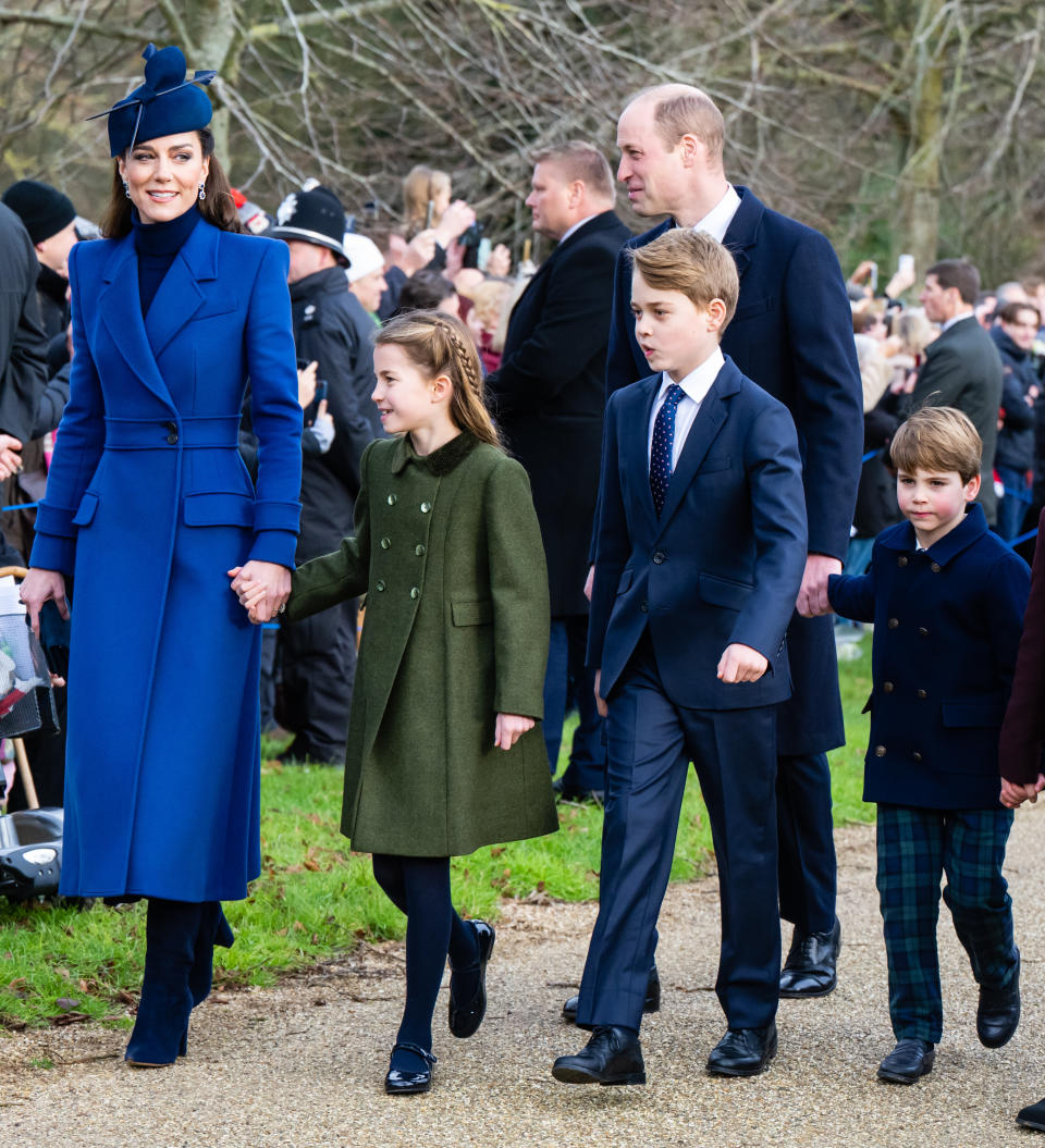 Kate Middleton in a blue coat and hat, walking with Prince William and their children, all dressed in formal attire