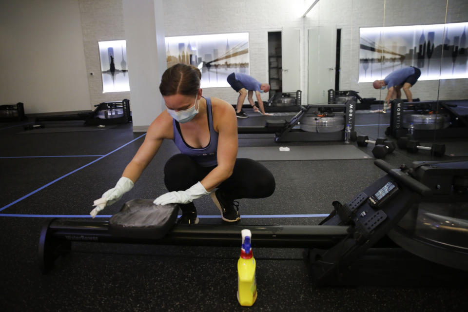 Employee of CITYROW Atlanta Midtown, Ellie Klarl, cleans the equipment after a class as gyms reopen with limited members on Saturday, May 16, 2020, amid the COVID-19 virus in Atlanta. Big box gyms and local fitness studios are reopening under a patchwork of protocols based on state and local guidance, but most are following some basic protocol. (AP Photo/Brynn Anderson)