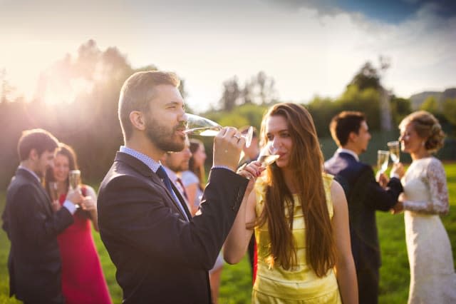 Wedding guests drinking champagne while the newlyweds clinking glasses in the background