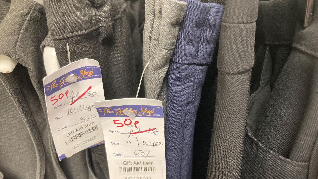 A close up image of a rail of grey and navy blue school trousers with tags on them which say 50p. They previously said £2.50 but that number has been crossed out.