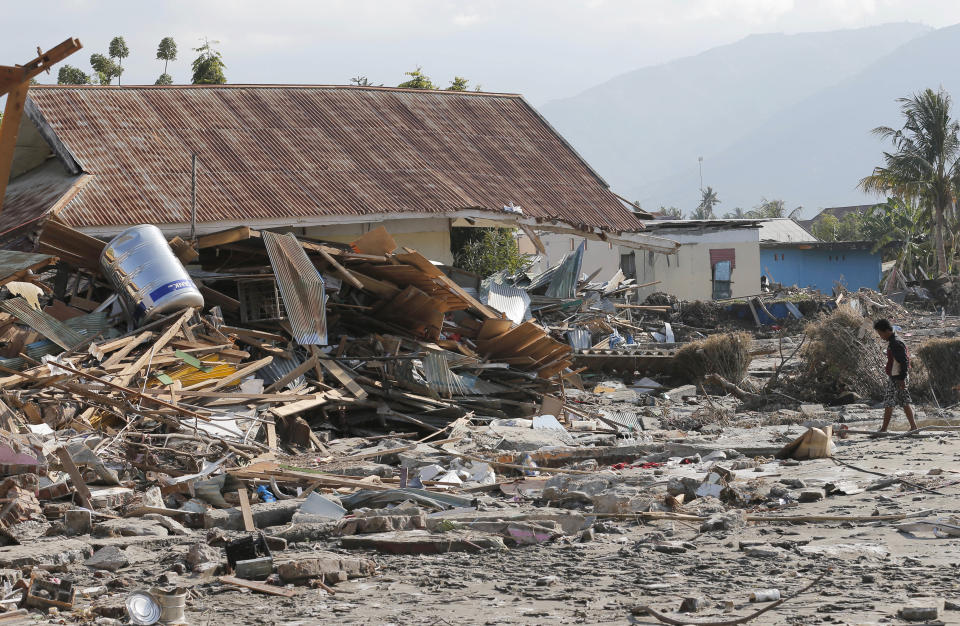 A man walks by houses damaged following a massive earthquake and tsunami at Talise beach in Palu, Central Sulawesi, Indonesia, Monday, Oct. 1, 2018. Bright-colored body bags were placed side-by-side in a freshly dug mass grave Monday, as a hard-hit Indonesian city began burying its dead from the devastating earthquake and tsunami. (AP Photo/Tatan Syuflana)
