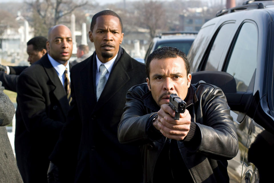 Men in suits and one in a jacket pointing a gun