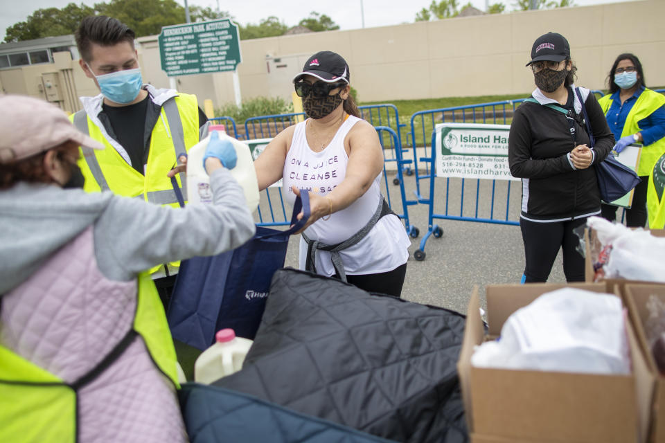 This Thursday, May 28, 2020, photo shows volunteers giving food to two women wearing Fendi logo face masks during a food distribution drive sponsored by Island Harvest Food Bank in Valley Stream, N.Y. (AP Photo/Mary Altaffer)