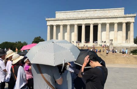 Tourists use umbrellas to try to keep cool in the sun in front of the Lincoln Memorial, on a day when the temperature was forecast to reach 99 degrees F, in Washington