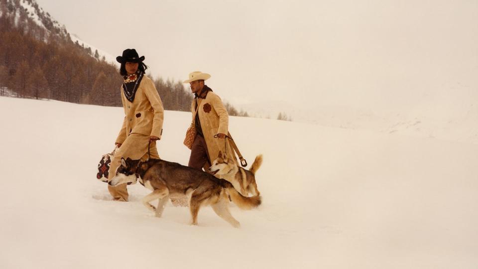 two men in coats and hats with a dog in the snow