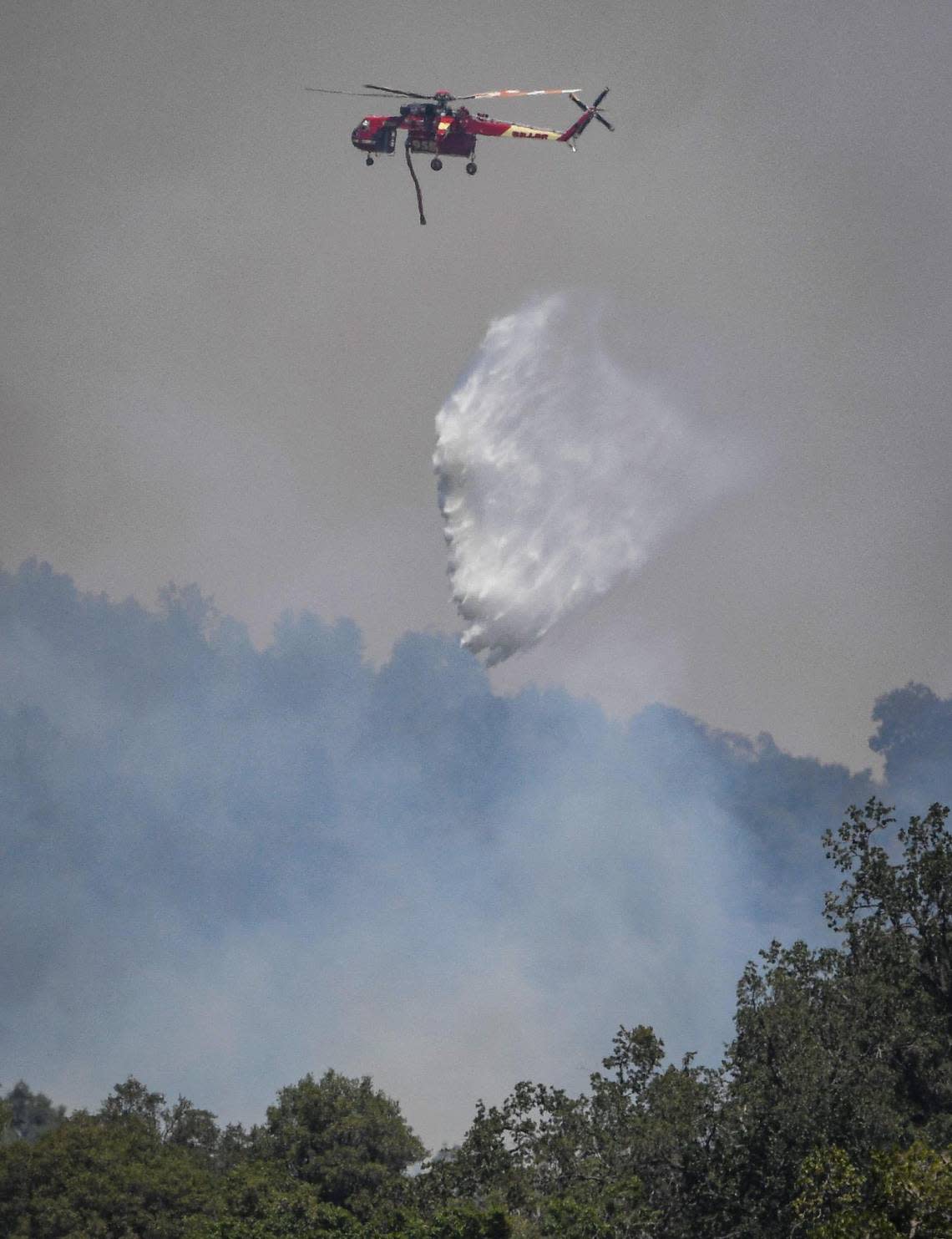 A helicopter tanker drops water on the Oak Fire burning in an area east of Mariposa on Saturday, July 23, 2022.