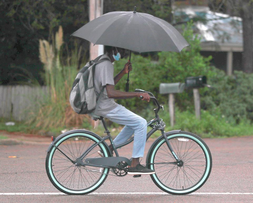 A bicyclist uses an umbrella to keep the rain off their head on Sept. 14, 2020, in Panama City Beach. The Bay County Commission has delayed several bicycle lane projects because of the rising cost of materials.