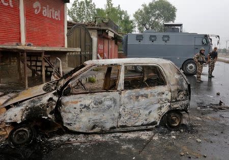 Policemen stand guard next to the wreckage of a vehicle that was damaged during a protest on Thursday evening, during a curfew in Srinagar July 15, 2016. REUTERS/Danish Ismail