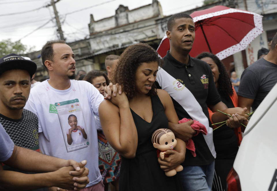 Vanessa Francisco Sales, carrying a doll that belonged to her 8-year-old daughter Ágatha Sales Felix, holds the hand of her husband Adegilson Felix, second from left, as they walk in their daughter's funeral procession to the cemetery in Rio de Janeiro, Brazil, Sunday, Sept. 22, 2019. Félix was hit by a stray bullet Friday amid what police said was shootout with suspected criminals. However, residents say there was no shootout, and blame police. (AP Photo/Silvia Izquierdo)