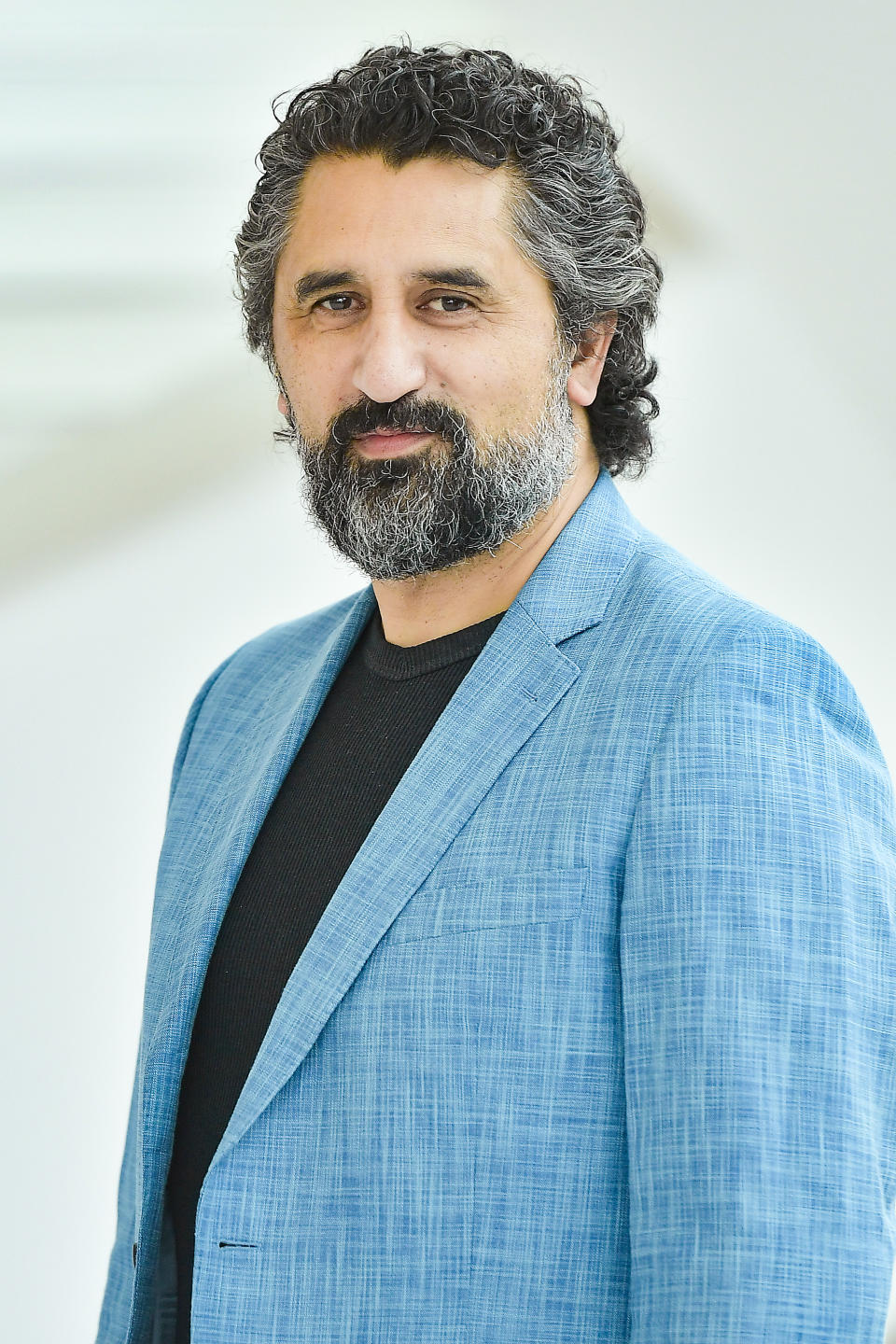 Cliff Curtis in a light blue jacket smiling with a beard