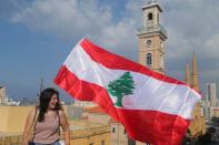 A demonstartor holds a Lebanese flag as she stands on a roof of a building during a protest targeting the government over an economic crisis, in Beirut