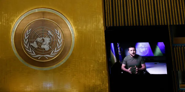 Symbol of United Nations next to screen showing feed of Ukrainian President Volodymyr Zelenskyy