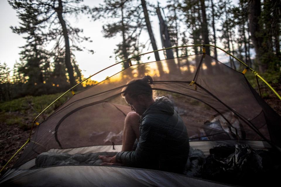 A man sits in a small tent and rubs his feet as the sun sets.