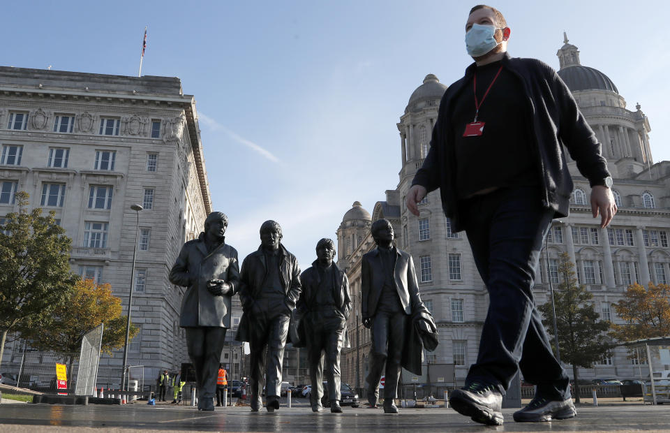 FILE - In this Wednesday, Oct. 14, 2020 file photo, a man wearing a face mask walks past a statue of the Beatles, as new measures across the region are set to come into force in Liverpool, England. A half-million people in the city of Liverpool will be regularly tested for COVID-19 in Britain’s first citywide trial of widespread, rapid testing that the government hopes will be a new weapon in combatting the pandemic. The government said in a statement Tuesday that testing will begin later this week at sites throughout the city using a variety of technologies, including new methods that can provide results in an hour or less. Everyone who lives or works in the city in northwestern England will be offered the test, regardless of whether they have symptoms. (AP Photo/Frank Augstein, File)