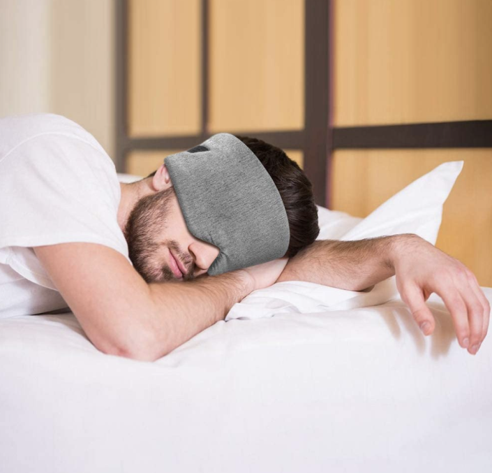ชายนอนบนเตียงสีขาวสวม Cotton Sleep Mask สีเทา (ภาพผ่าน Amazon)