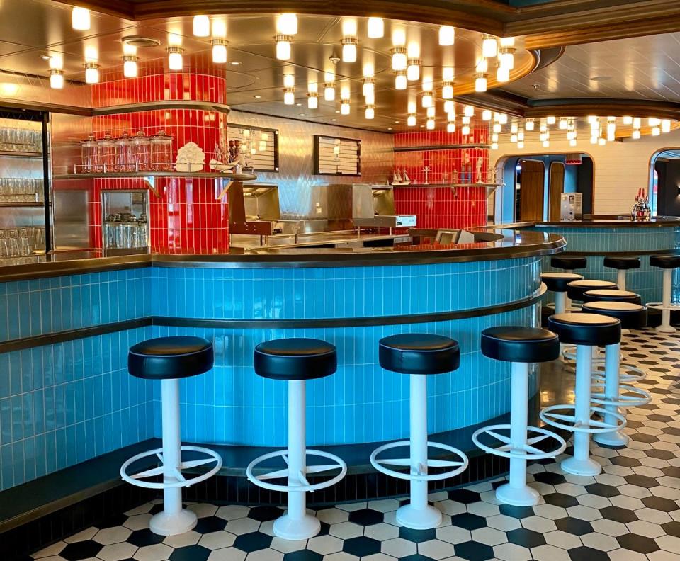 The Social Club diner on Virgin Voyages scarlet lady: Empty stools on a checkerboard floor in front of a bar