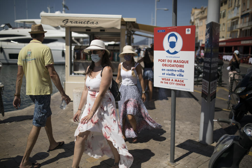 Tourists walk by a sign instructing pedestrians to respect a mandatory face mask requirement in Saint-Tropez, southern France, Saturday Aug 8, 2020. The glamorous French Riviera resort of Saint-Tropez is requiring face masks outdoors starting Saturday, threatening to sober the mood in a place renowned for high-end, free-wheeling summer beach parties. (AP Photo/Daniel Cole)